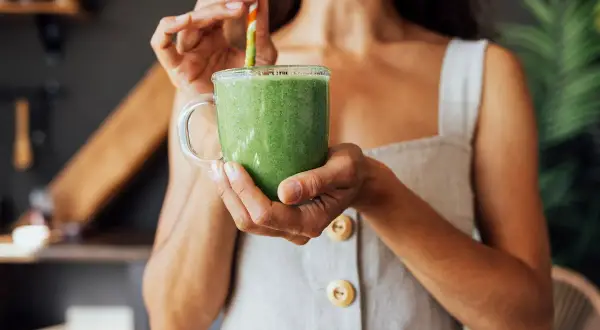 Donna sorseggia un frullato verde, un'ottima opzione su cosa bere per dimagrire.