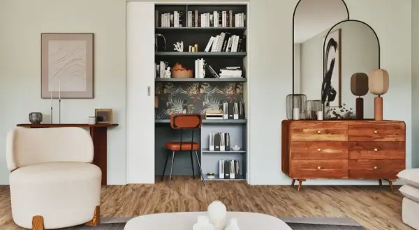 Un bureau placard aménagé avec une chaise orange, des étagères remplies de livres et un papier peint tropical.