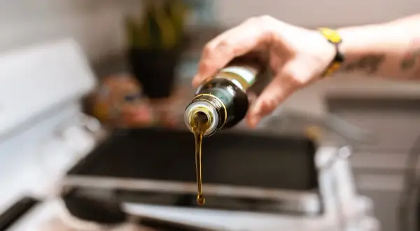 Una mano versa olio extravergine di oliva da una bottiglia su una piastra.