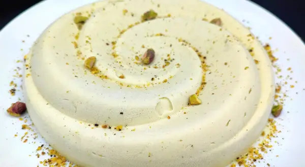 Delizioso semifreddo al pistacchio, decorato con granella e pistacchi interi, servito su un piatto bianco.