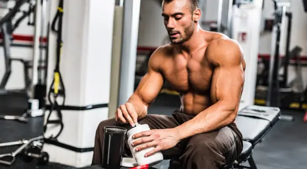 Muskulöser Mann im Fitnessstudio bereitet Proteinshake zu. Was hilft beim Muskelaufbau? Richtige Ernährung und Supplemente sind wichtig.