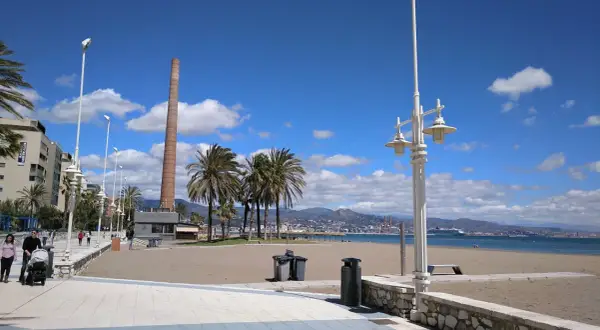 Paseo marítimo con palmeras y chimenea industrial. La playa Misericordia, ideal para llegar y disfrutar del mar.