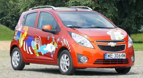 Pomarańczowy Chevrolet Spark 2010 z kolorowymi, abstrakcyjnymi wzorami na karoserii.