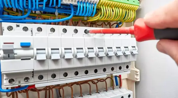 Instalacja uzbrojenia rozdzielni elektrycznej. Ręka z czerwonym śrubokrętem dokręca śrubę. Sprawdź uzbrojenie rozdzielni elektrycznej cena.