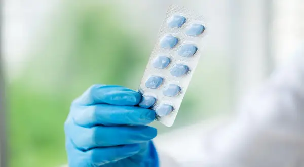 Ręka w niebieskiej rękawiczce trzyma opakowanie z niebieskimi tabletkami, które mogą pomóc w problemach z potencją.