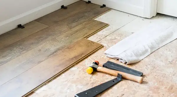 Laying LVP flooring parallel to the longest wall is a common practice. Tools like a rubber mallet and pry bar are ready for installation.
