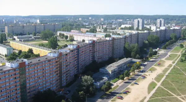 Długi falowiec gdański wzdłuż ulicy, z wieloma oknami i balkonami, otoczony zielenią i innymi budynkami.