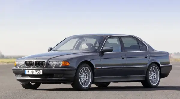 Ciemnoszary sedan BMW serii 7 (E38) z silnikiem V12 na tle nieba.