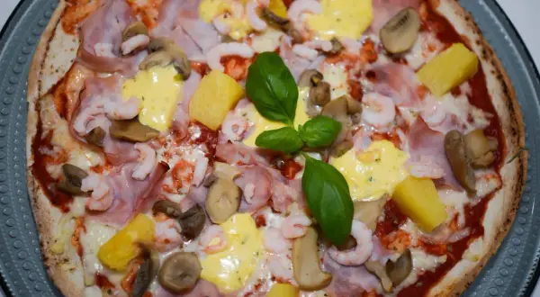 En läcker pizza med räkor och skinka, toppad med ananas, champinjoner och en krämig sås. En riktig smakupplevelse!