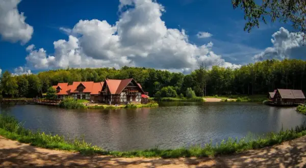 Idealne miejsce na długi weekend w sierpniu: urokliwe domki nad jeziorem, otoczone lasem, z pięknym niebem i chmurami.