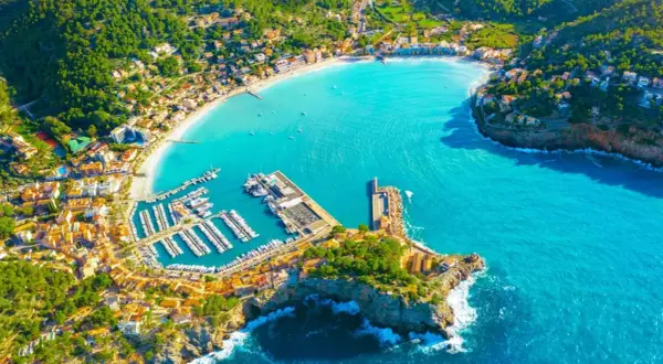 Vacker vy över en turkos bukt med en hamn full av båtar och en stad som klättrar uppför kullarna. En drömsemester i Palma de Mallorca.