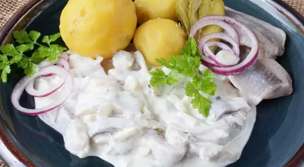 Marinierter Hering in cremiger Sauce mit Salzkartoffeln, Gurken und Zwiebelringen garniert.