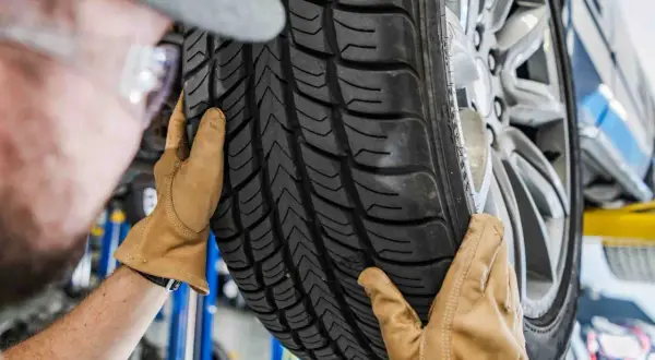 Mechanik w rękawiczkach ogląda bieżnik nowej opony samochodowej.