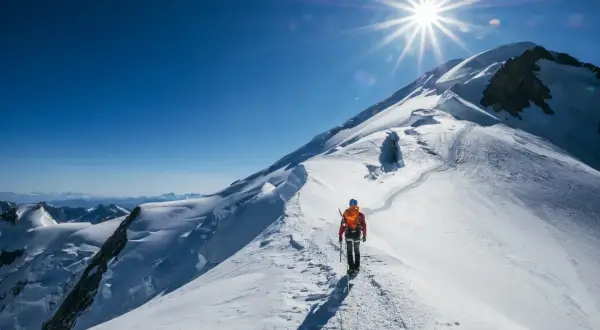 Un alpiniste solitaire progresse sur une crête enneigée, le soleil éclatant au-dessus du sommet du Mont-Blanc.