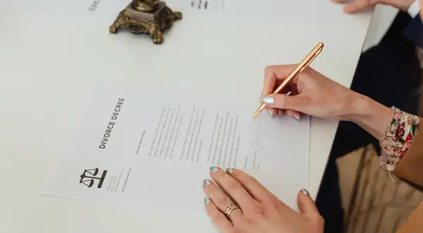 Kobieta podpisuje dokument "DIVORCE DECREE". Wniosek o rozwód można pobrać online.