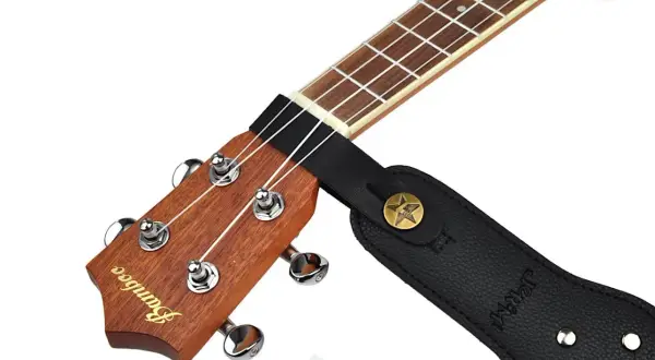 Czarny pasek do gitary przymocowany do gryfu ukulele. Pokazuje, jak przyczepić pasek do gitary, zaczepiając go o główkę instrumentu.