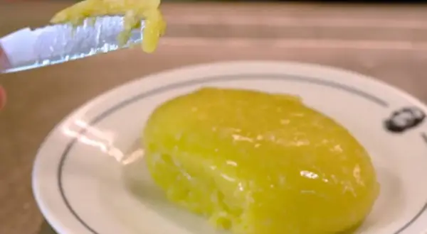 Un trozo de alioli casero untado en un cuchillo, listo para probar la deliciosa salsa sobre un plato blanco.