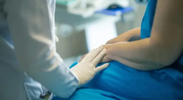 Lekarz w białej rękawiczce delikatnie dotyka dłoni pacjenta. Rozmowa o tym, porfiria co to, trwa w tle.
