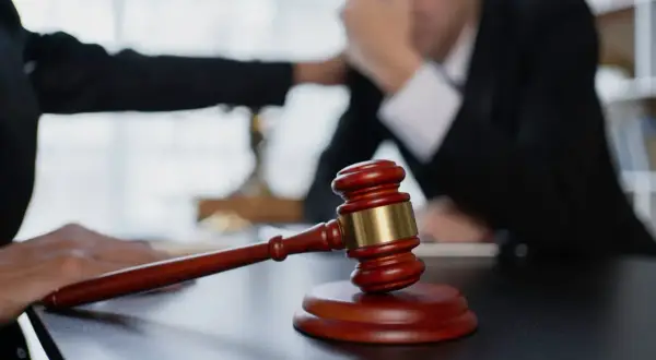 Młotek sędziowski na stole. Dłoń kładzie się na ramieniu zmartwionego mężczyzny, sugerując, że prawa dłużnika ważniejsze niż wierzyciela.