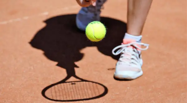 Tenisista przygotowuje się do uderzenia piłki. Cień rakiety i piłki na korcie przypomina, co to ATP.