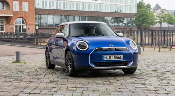Mini Cooper SE azul aparcado en calle adoquinada, con edificios modernos de fondo. Su autonomía eléctrica inspira libertad.