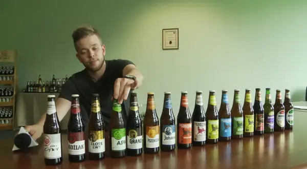 Mężczyzna wybiera piwo bez drożdży z rzędu butelek. Widać różne rodzaje piw, m.in. APA, Koźlak, Złote Lwy.