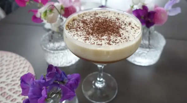 En krämig drink med chokladströssel, perfekt för en stunds avkoppling. Kanske en Kaffe Karlsson? Blommor i rosa och lila ger en vacker inramning.