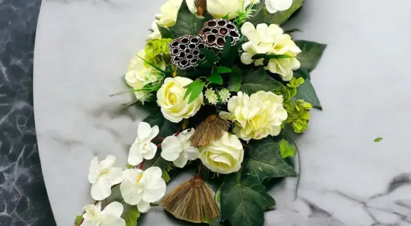 Eleganckie kompozycje funeralne z białych róż, storczyków i ozdobnych łusek lotosu na marmurowym tle.