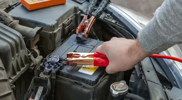 Ręka podłącza kable rozruchowe do akumulatora samochodowego.