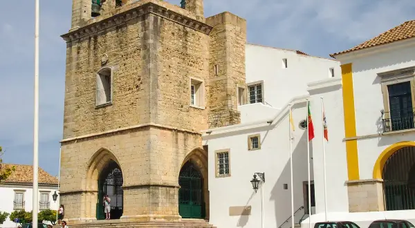 Historisches Gebäude mit Glockenturm in der faro portugal altstadt. Weiße Gebäude mit gelben Akzenten und portugiesische Flaggen.