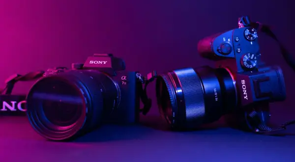 Dwa aparaty Sony, jeden z obiektywem 70-200mm, drugi z 85mm f/1.8. Różne rodzaje aparatów fotograficznych w neonowym świetle.