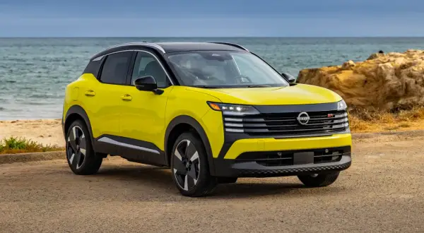 Żółty Nissan Kicks z czarnym dachem stoi na plaży przy spokojnym morzu.