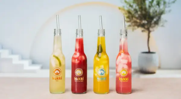 Vier bunte Kukki Cocktails mit Eis und Strohhalmen, bereit zum Auftauen und Genießen.