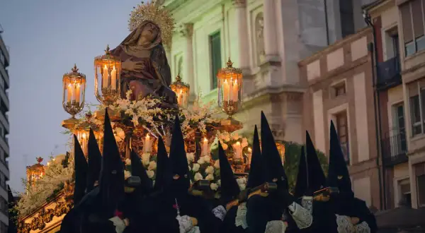 Figuras encapuchadas portan un paso con la Virgen, iluminado por velas, durante las procesiones de Sábado Santo.