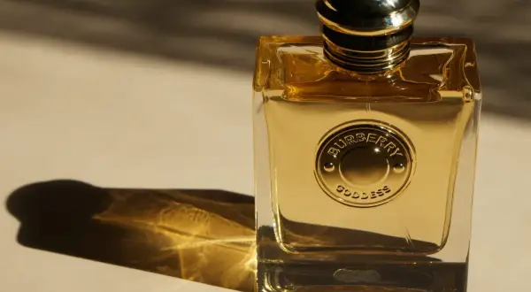 Złota butelka perfum Burberry Goddess, lśniąca w świetle, z wytłoczonym logo.