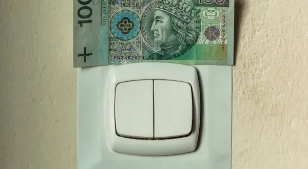 Sto złotych na włączniku światła symbolizuje wysokie rachunki za prąd, np. w taryfie G11 PGE.