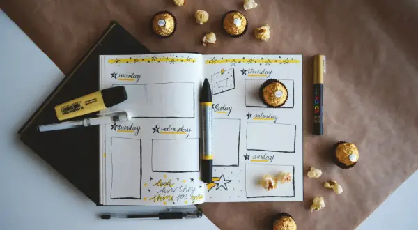Plan rozwoju osobistego przykład: otwarty notatnik z kalendarzem tygodniowym, pisaki, czekoladki i popcorn.