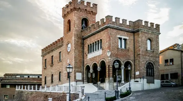 Edificio in mattoni rossi con torre dell'orologio e merlature, un esempio di cosa vedere a Mondolfo.