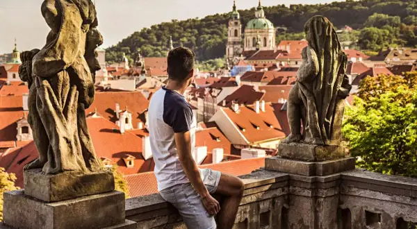 Un homme contemple les toits de Prague, une ville d'Europe aux charmes intemporels, depuis un balcon orné de statues.