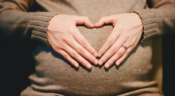 Mani a cuore sul pancione, simbolo di maternità flessibile e amore in attesa.