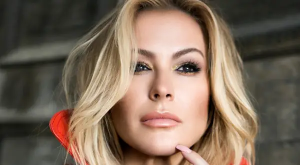 Zbliżenie na twarz Anastacii z blond włosami, złotym makijażem oczu i czerwoną stójką.