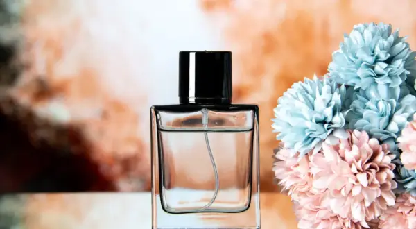 Elegancka butelka perfum z czarną nakrętką, obok bukiet pastelowych kwiatów. Chcesz wiedzieć, jak sprawdzić oryginalność perfum?