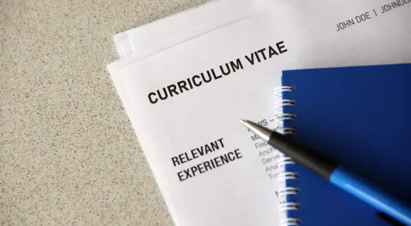 Długopis leży na dokumentach z nagłówkiem "CURRICULUM VITAE". Widoczna jest sekcja "RELEVANT EXPERIENCE" oraz klauzula CV po angielsku.
