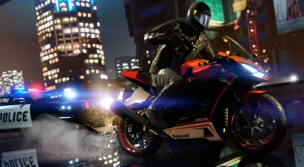Motocyklista w kasku ucieka przed radiowozem policyjnym w nocnym mieście.