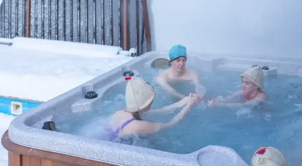 Rodzina cieszy się kąpielą w jacuzzi zimą. Od jakiego wieku można korzystać z jacuzzi? Odpowiedź zależy od dziecka, ale ta rodzina świetnie się bawi!