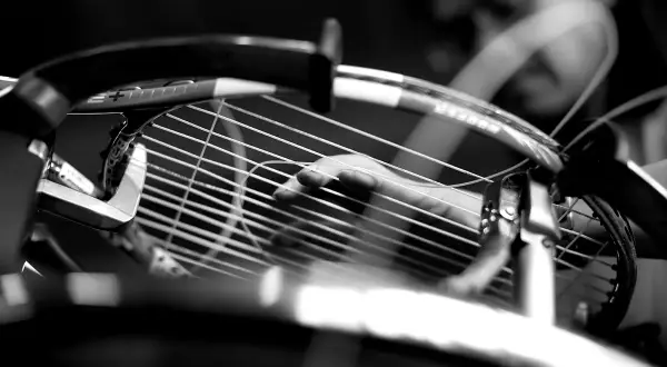 Mano che regola la tensione delle corde di una racchetta da tennis, un dettaglio cruciale per la performance.