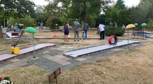Familien spielen Minigolf Gummersbach. Bunte Bahnen mit Hindernissen wie einem roten Reifen laden zum Spiel ein.