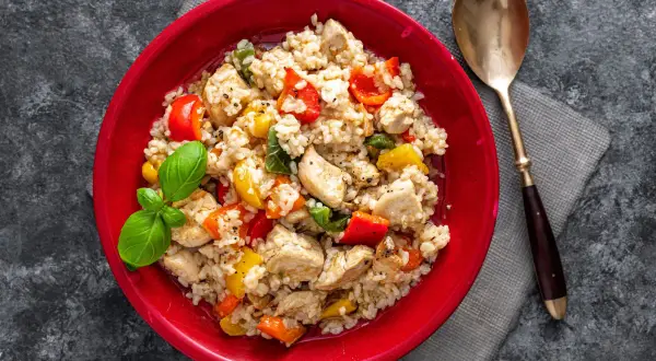 Pyszne risotto z kurczakiem, kolorową papryką i świeżą bazylią, podane w czerwonej misce.