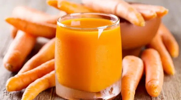 Succo d'arancia brillante circondato da carote fresche, un concentrato di vitamine e benefici per la salute.