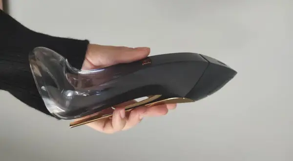 Dłoń trzyma flakon perfum Carolina Herrera Good Girl Legere, przypominający czarny szpilkę ze złotym obcasem.